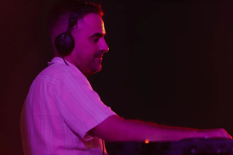 A DJ in a patterned shirt mixing under magenta light