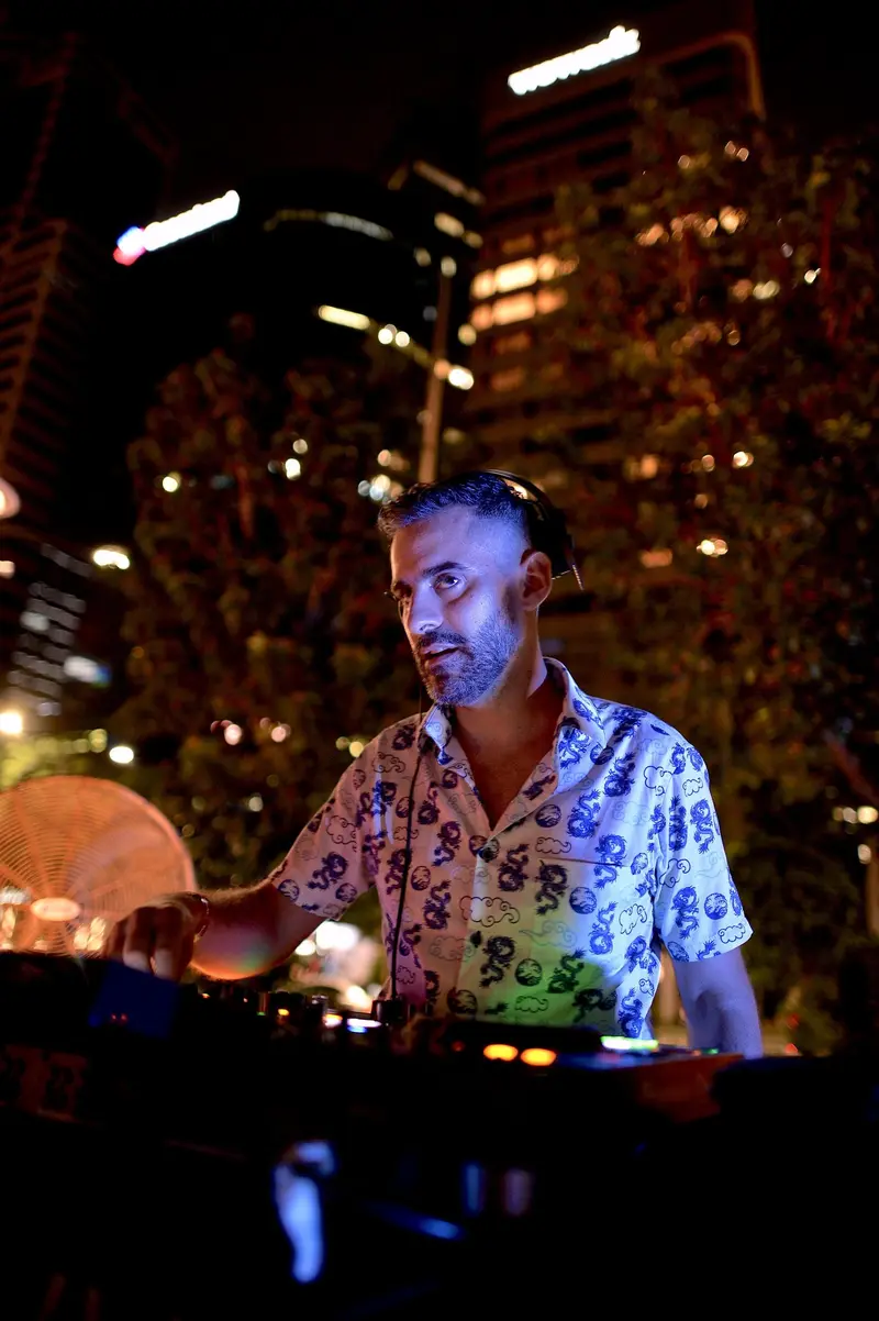 Driguo in the booth at night, lit from the decks