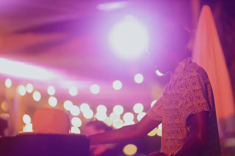 A guest DJ bathed in magenta stage glow with string lights behind