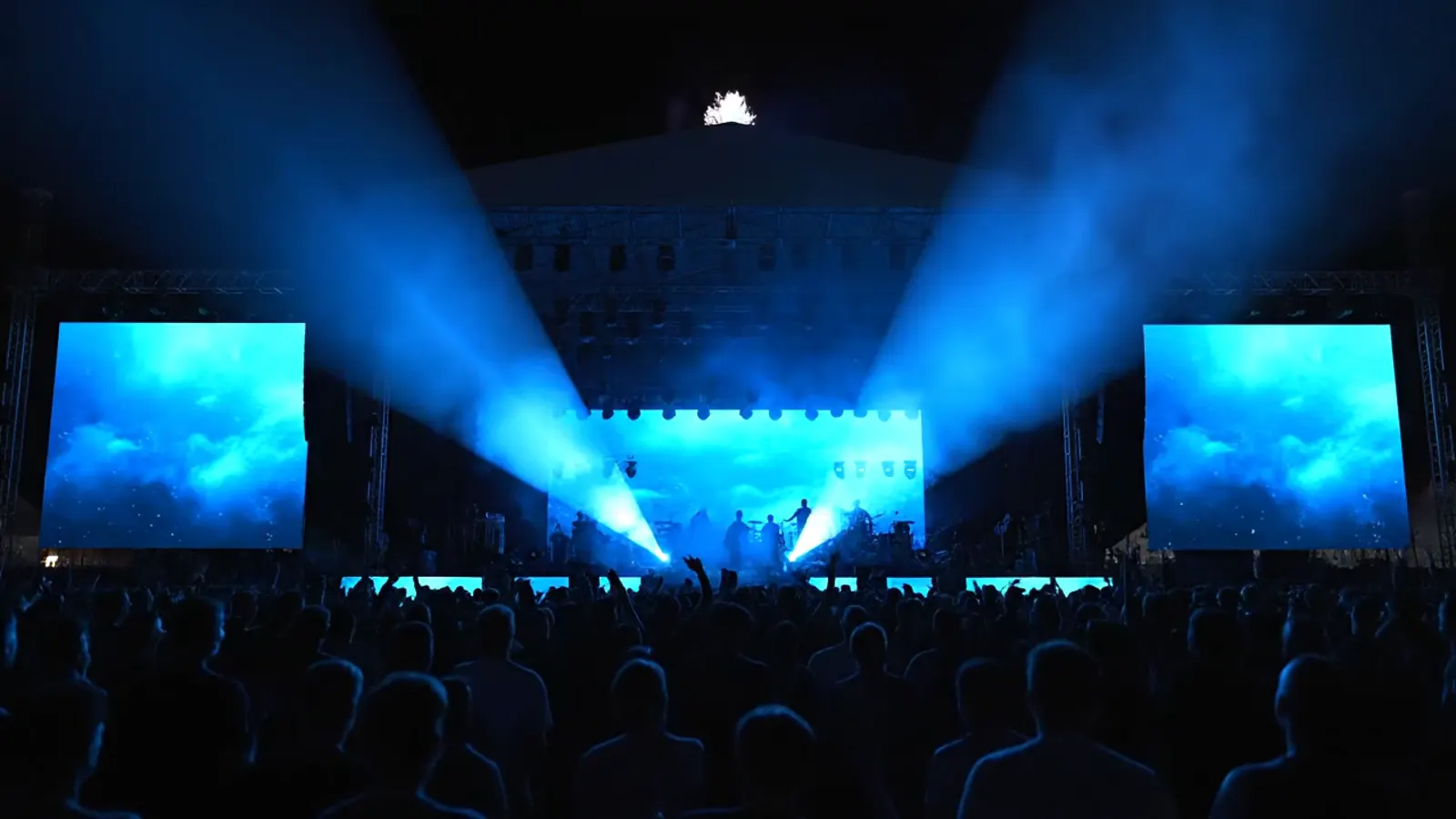 Blue light beams sweeping over an outdoor stage and crowd